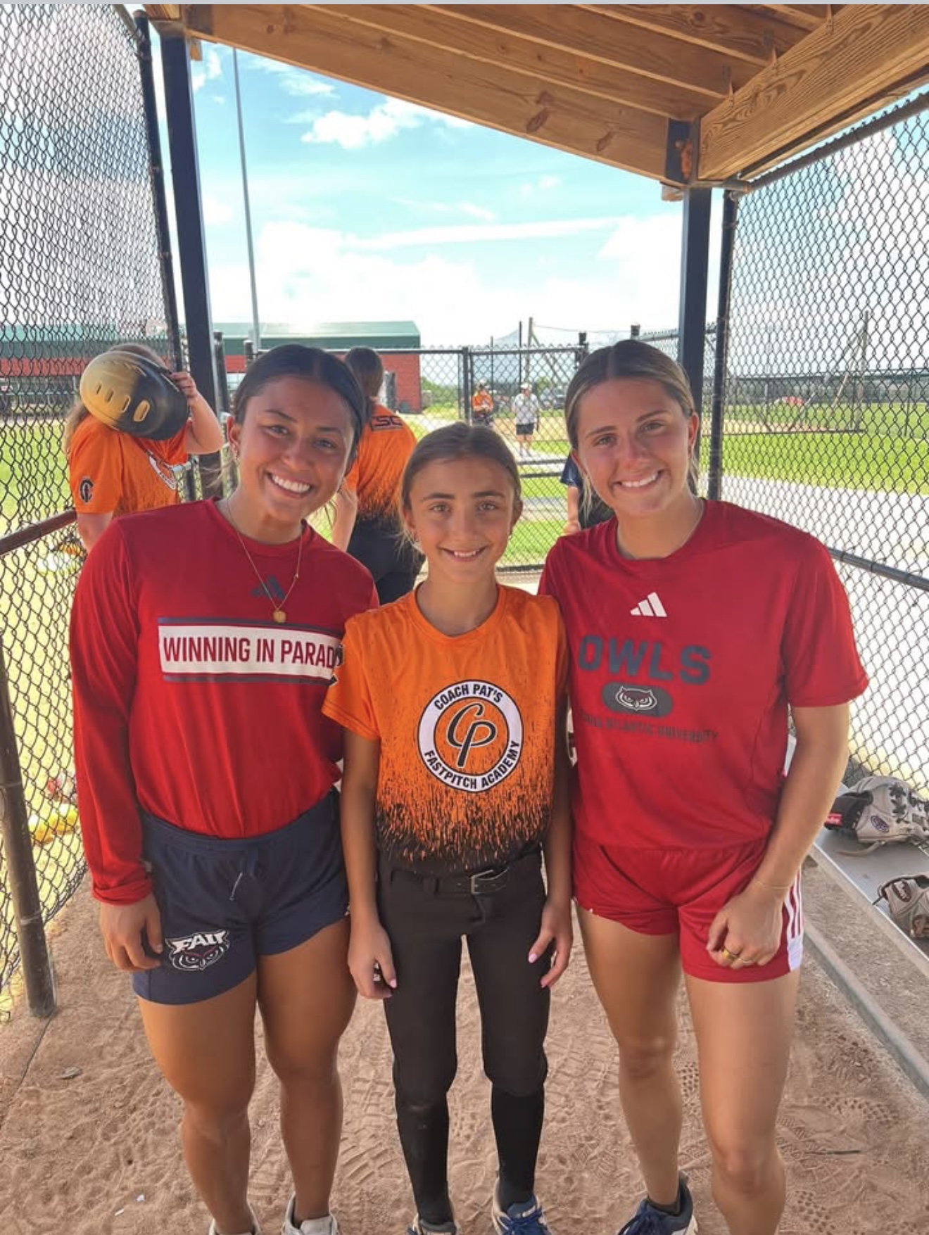 Three softball players smiling in dugout