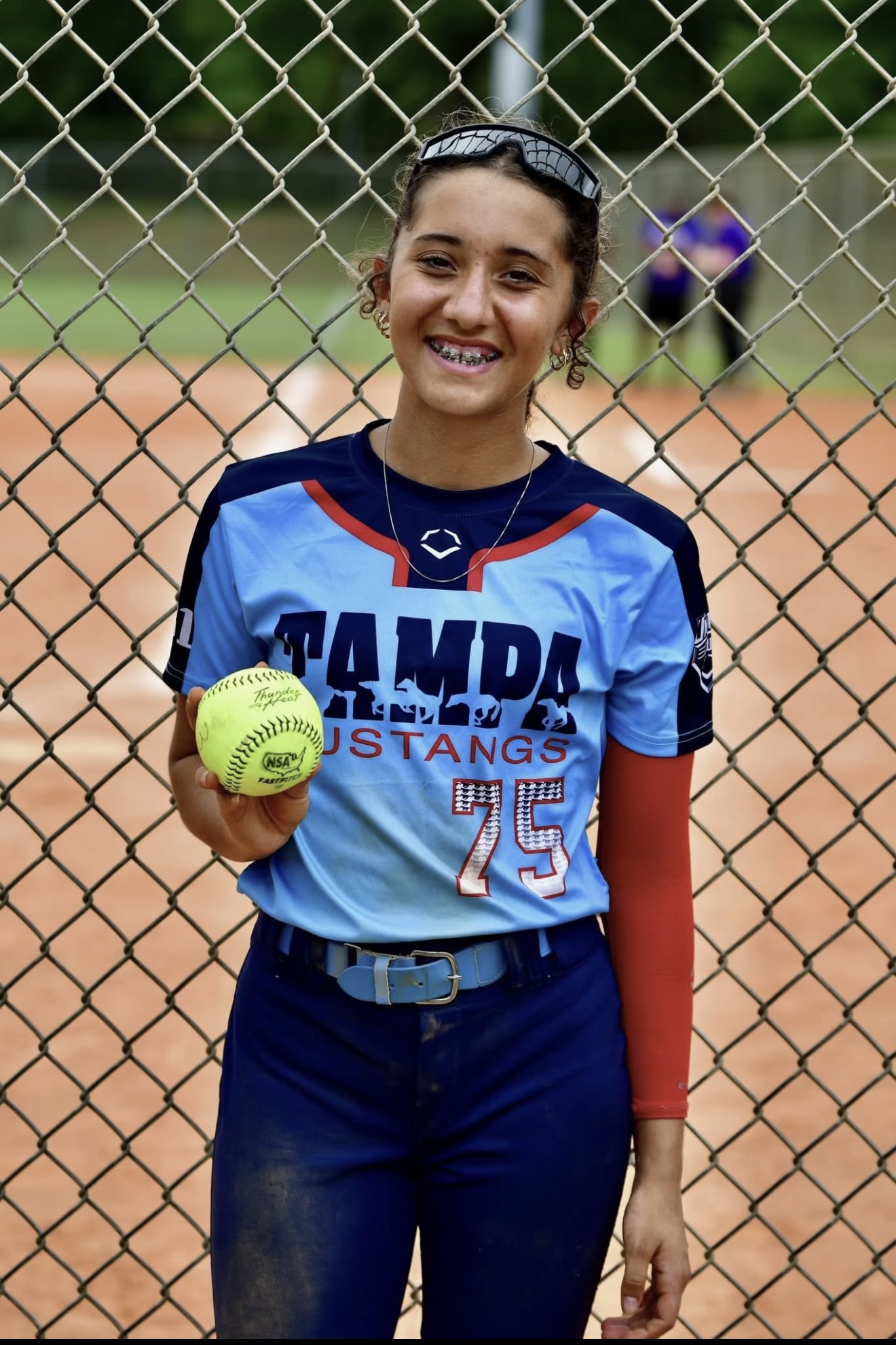 Smiling softball player holding yellow softball by fence